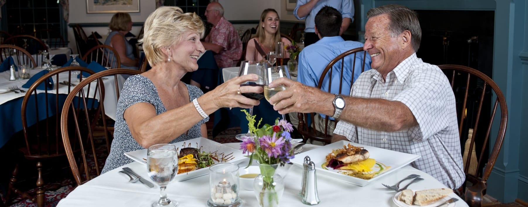 Older couple toasting wine glasses at dinner.