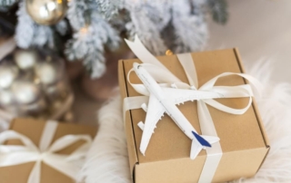 A present with a plane and bow on it next to a Christmas tree, indicating that the gift is the gift of travel